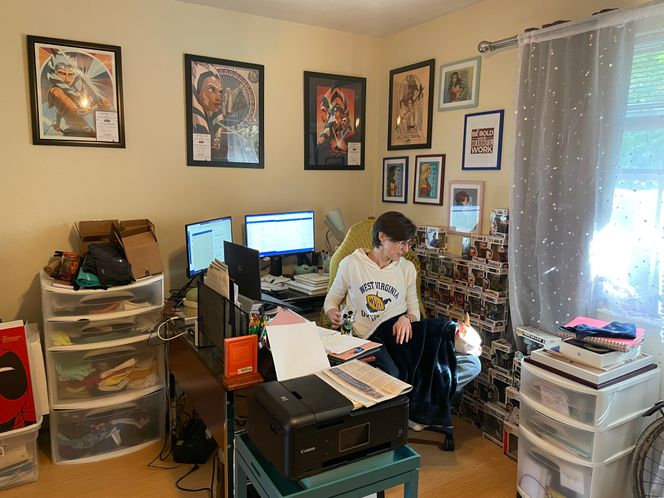 Nora working at her desk with two monitors and books spread around her. 
